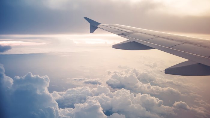 Cropped image of an airplane, only showing the wing while in flight above the clouds.